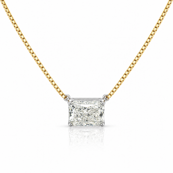 A radiant cut diamond pendant necklace on a gold box chain, set in a silver-colored prong setting against a white background with a soft reflection. – Assay Jewelers